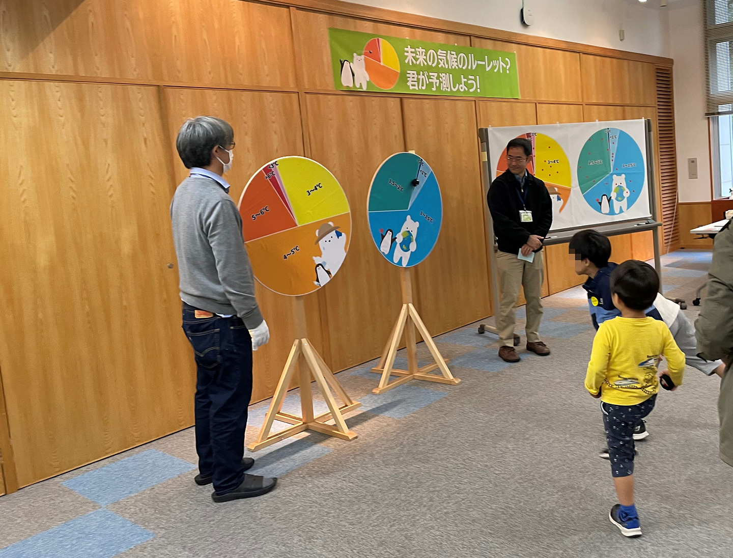 「未来の気候のルーレット？君が予測しよう！」で塩竈室長（左）と小倉室長（右）が見守る中、参加者がルーレットに向かってボールを投げているところ。